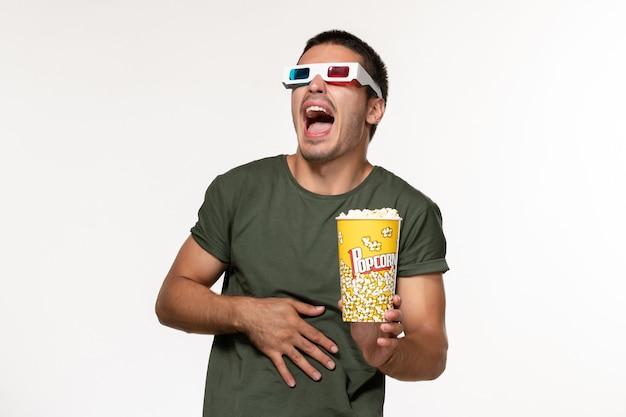 Widok z przodu młody mężczyzna w zielonej koszulce trzymający popcorn w d okulary przeciwsłoneczne oglądający film na jasnobiałej powierzchni film samotne kino męskie filmy