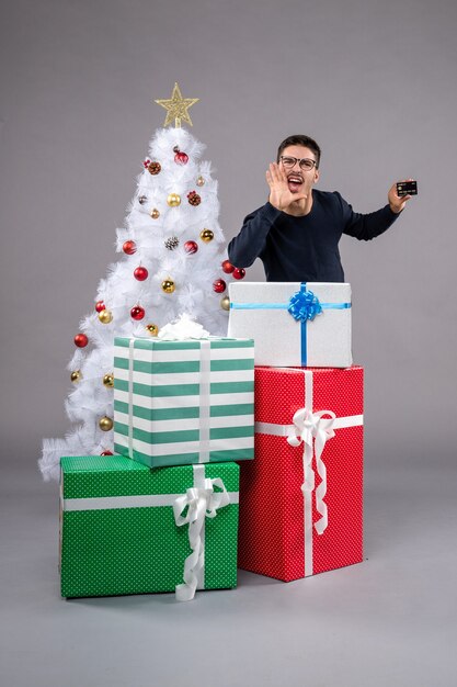 Widok z przodu młody mężczyzna z kartą bankową na szarej podłodze prezent świąteczny nowy rok