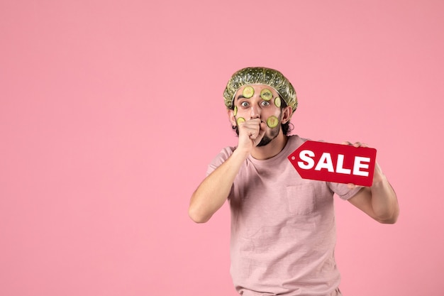 widok z przodu młody mężczyzna z maską na twarzy trzymając tabliczkę sprzedaży na różowym tle