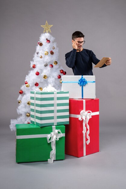 Widok z przodu młody mężczyzna z prezentami i kopertą na szarym biurku nowy rok boże narodzenie człowieka