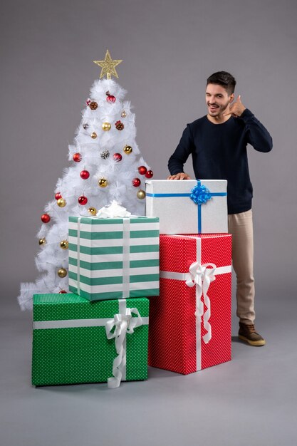 Widok z przodu młody mężczyzna z prezentami świątecznymi na szarej podłodze prezent świąteczny nowy rok