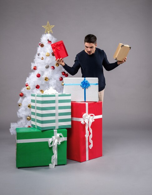 Widok z przodu młody mężczyzna z świątecznymi prezentami na szarym biurku prezent nowy rok boże narodzenie ludzki