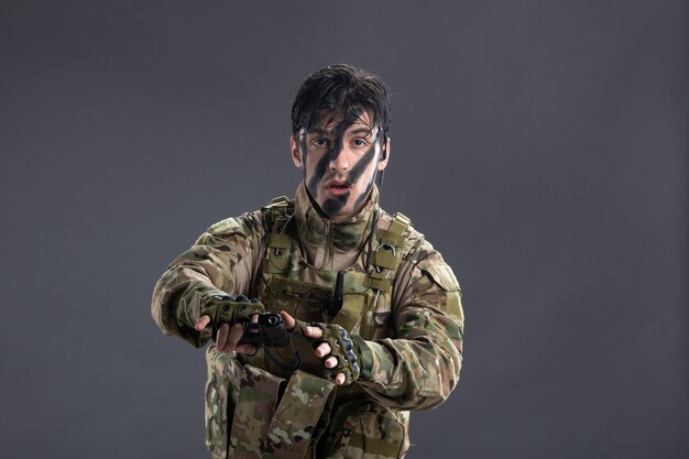 Widok z przodu młody żołnierz poddający się w kamuflażu z pistoletem na ciemnej ścianie