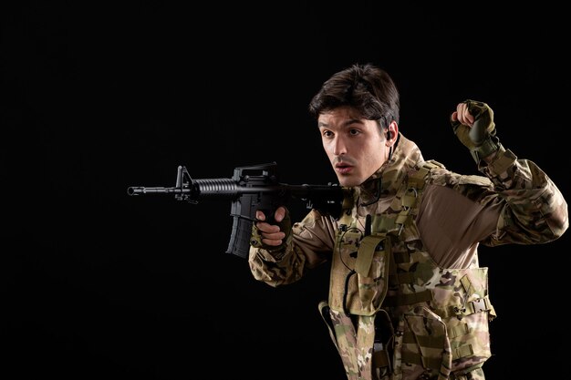 Bezpłatne zdjęcie widok z przodu młody żołnierz w mundurze celujący z karabinu na czarnej ścianie