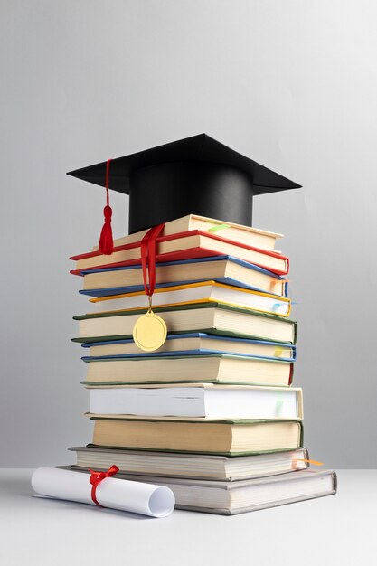 Widok z przodu na ułożone w stos książki, czapkę maturalną i dyplom na dzień edukacji