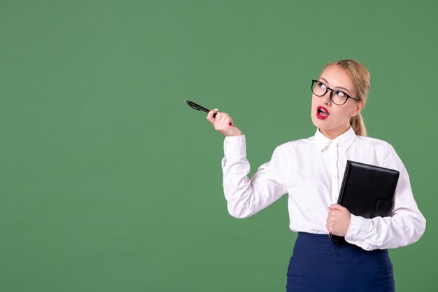 Widok z przodu nauczycielka w okularach przeciwsłonecznych z notatnikiem i długopisem na zielonym tle pieniądze praca kobieta książka student szkoła dokument lekcja nauka