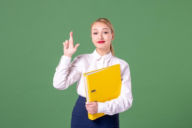 Widok z przodu nauczycielka w surowych ubraniach z żółtymi plikami na zielonym tle studentka uniwersytetu kobieta książka biblioteka szkoła lekcja pracy