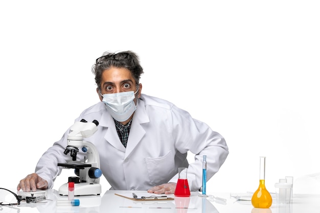 Widok z przodu naukowca w średnim wieku w specjalnym białym garniturze przy użyciu mikroskopu