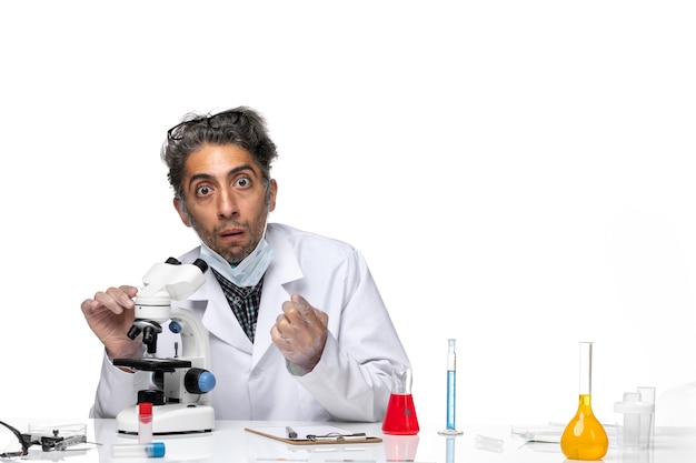 Widok z przodu naukowiec w średnim wieku w białym garniturze medycznym, próbujący użyć mikroskopu