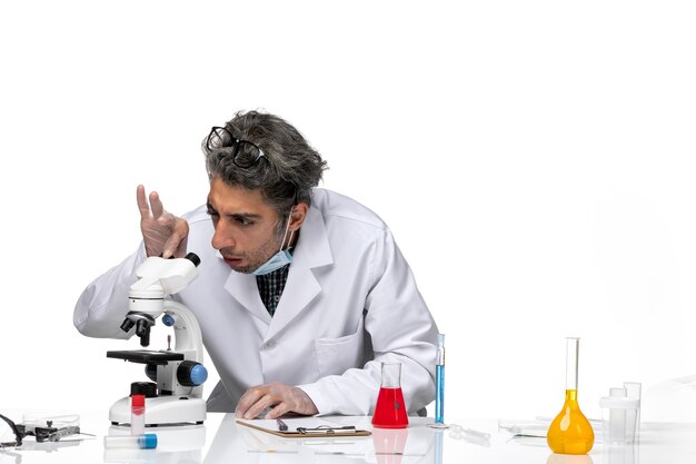 Widok z przodu naukowiec w średnim wieku w białym garniturze medycznym przy użyciu mikroskopu