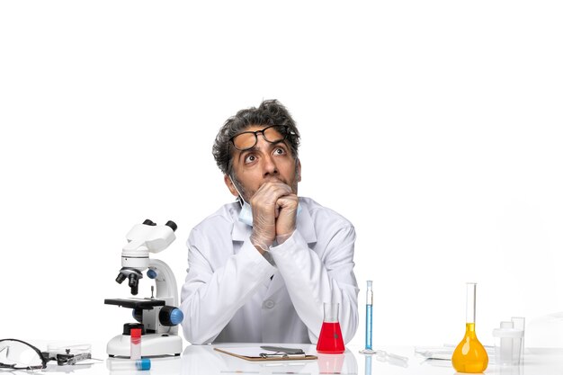 Widok z przodu naukowiec w średnim wieku w specjalnym białym garniturze, siedzący przy stole z myśleniem o rozwiązaniach