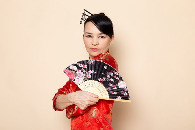 Widok z przodu piękna japońska gejsza w tradycyjnej czerwonej japońskiej sukience z paskami włosów stanowiących elegancki składany wentylator na ceremonii kremowej w Japonii