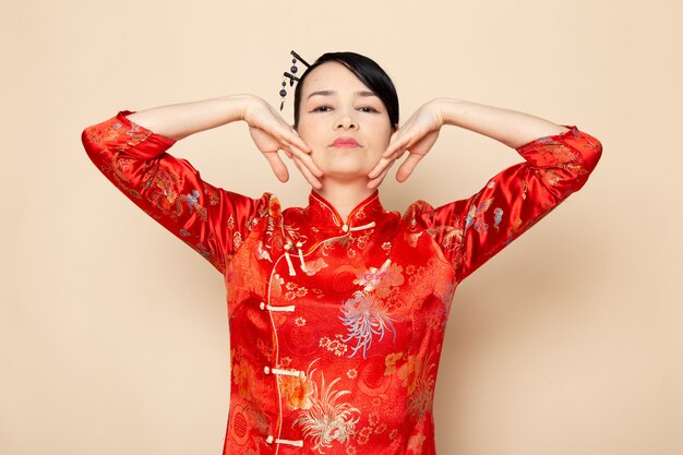 Widok z przodu piękna japońska gejsza w tradycyjnej czerwonej japońskiej sukni z włosami wystającymi z eleganckimi rękami na kremowej ceremonii zabawnej Japonii na wschód