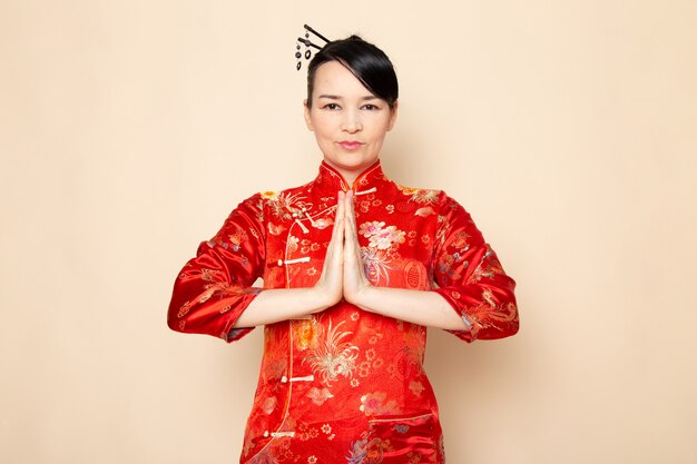 Widok z przodu piękna japońska gejsza w tradycyjnej czerwonej japońskiej sukni z włosami wystającymi z rękami stojącymi na kremowej ceremonii zabawnej Japonii na wschód