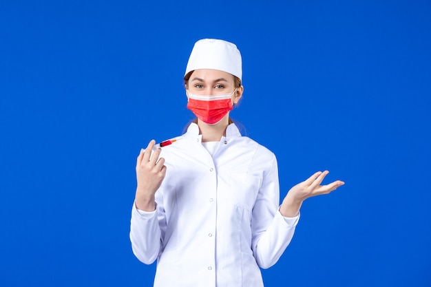 Widok z przodu pielęgniarka w białym garniturze medycznym z czerwoną maską i zastrzykiem w dłoniach na niebiesko