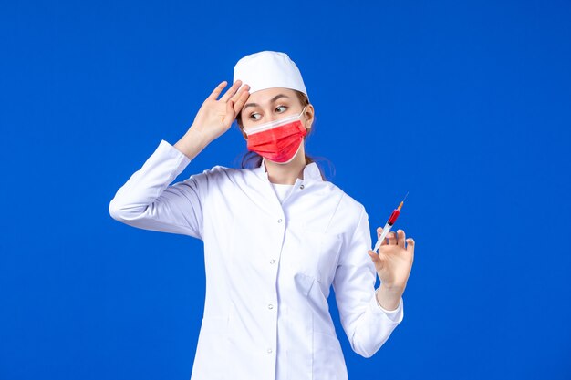 Widok z przodu podkreśliła pielęgniarka w białym garniturze medycznym z czerwoną maską i zastrzykiem w dłonie na niebiesko