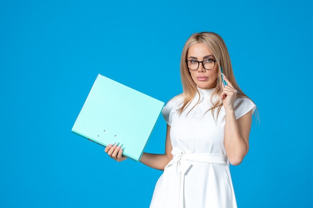 Bezpłatne zdjęcie widok z przodu pracownica w białej sukni trzymającej folder na niebieskiej ścianie