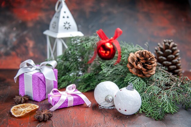 Widok z przodu prezenty bożonarodzeniowe gałęzie sosny z szyszkami bożonarodzeniowa piłka zabawki latarnia na ciemnoczerwonym na białym tle zdjęcie świąteczne