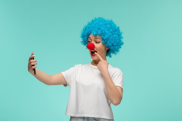 Widok z przodu prima aprilis szczęśliwa dziewczyna biorąca selfie wskazująca na usta z czerwonym nosem kostium klauna niebieskie włosy