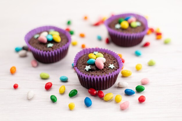 Widok z przodu pyszne ciasteczka w fioletowych formach z kolorowymi cukierkami na białych, cukierkowych cukierkach