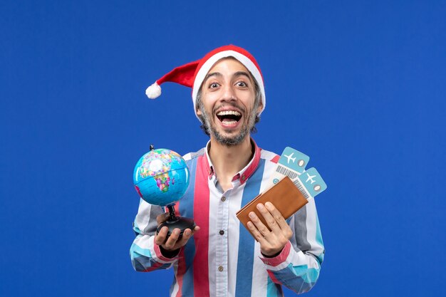 Widok z przodu regularny mężczyzna z biletami i kulą ziemską na niebieskim kolorze ściany wakacje nowy rok