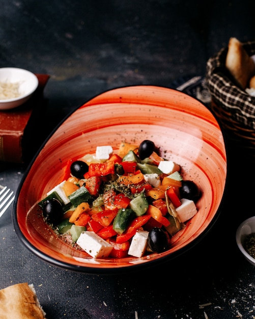 Widok z przodu sałatka grecka z oliwkami, pomidorami, białym serem i ogórkami wewnątrz czarnej płyty na ciemnej podłodze