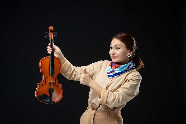 Widok z przodu skrzypaczka trzymająca skrzypce na ciemnej ścianie melodia instrument muzyczny kobieta koncert występ gra emocje