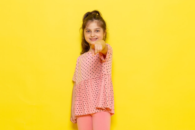 Bezpłatne zdjęcie widok z przodu słodkie małe dziecko w różowej sukience uśmiecha się i wskazuje