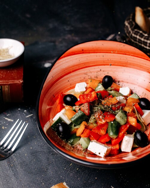 Widok z przodu smaczna sałatka grecka z warzywami i białym serem pokrojona w czarny talerz na ciemnym biurku