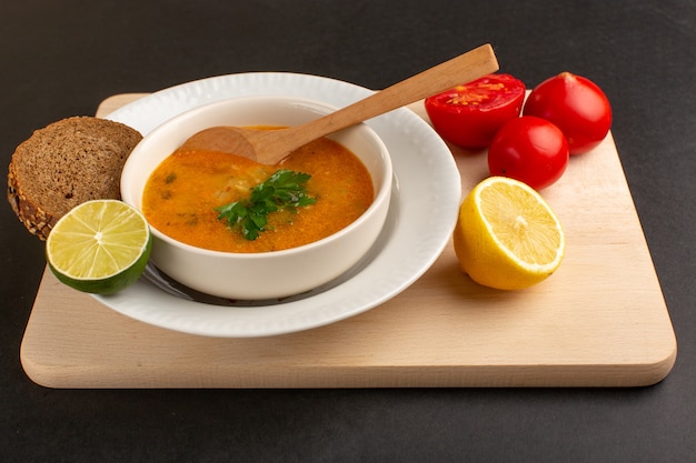Widok z przodu smaczna zupa jarzynowa wewnątrz płyty z pomidorami cytrynowymi bochenek chleba na ciemnym biurku.