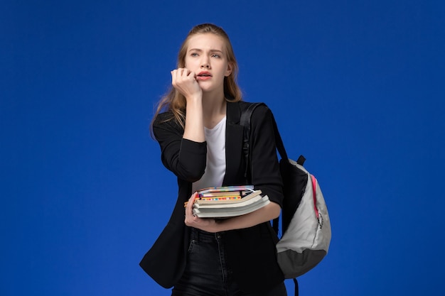 Bezpłatne zdjęcie widok z przodu studentka w czarnej kurtce na sobie plecak z książkami na lekcji college'u na jasnoniebieskiej ścianie