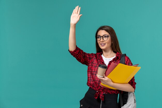 Widok z przodu studentki na sobie plecak z plikami i kawą na jasnoniebieskiej ścianie