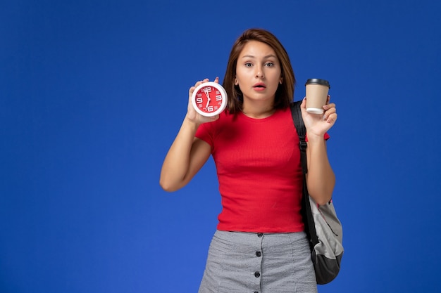 Bezpłatne zdjęcie widok z przodu studentki w czerwonej koszuli z plecakiem, trzymając zegary i kawę