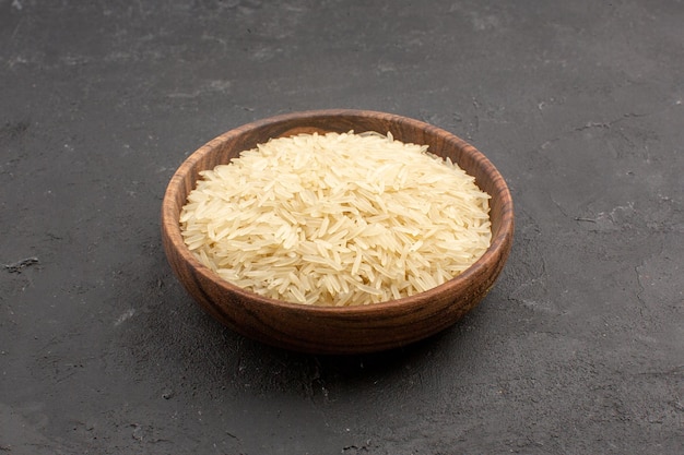 Widok z przodu surowego ryżu wewnątrz brązowego talerza na szarym polu