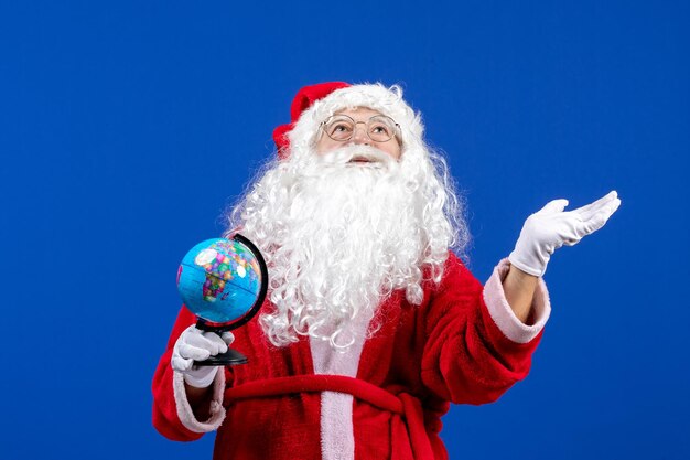 Widok z przodu święty mikołaj trzymający małą kulę ziemską na niebieskim kolorze święta bożego narodzenia nowy rok