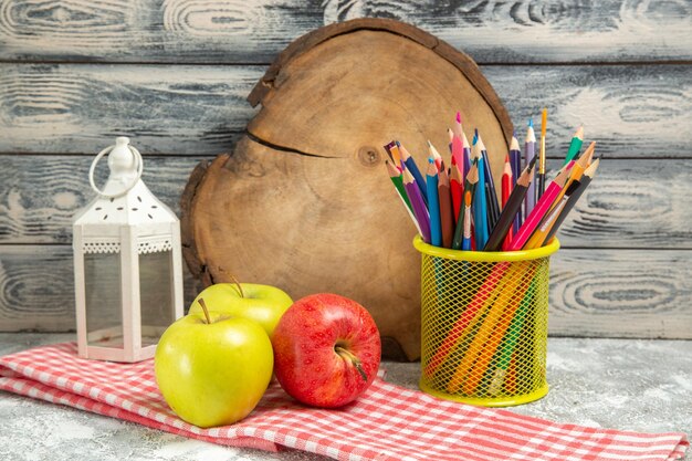 Widok z przodu świeże jabłka z kolorowymi ołówkami na szarym tle dojrzałe, aksamitne świeże owoce