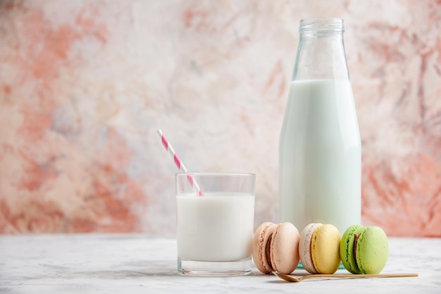 Widok z przodu świeżego mleka w szklanym kubku i otwartej butelce obok kolorowych pysznych makaroników na pastelowych powierzchniach