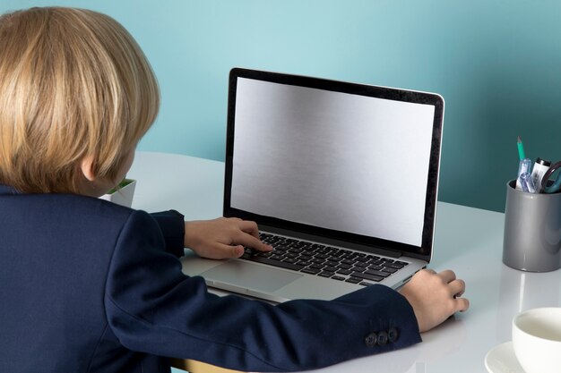 Widok z przodu uroczy chłopak w niebieskim klasycznym garniturze przed srebrną modą na laptopa