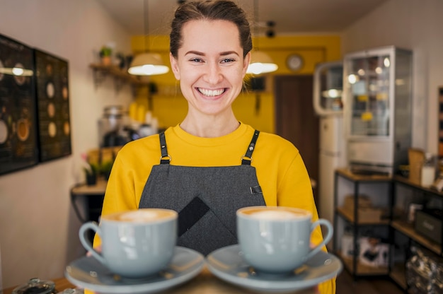 Bezpłatne zdjęcie widok z przodu uśmiechnięta barista serwująca filiżanki kawy