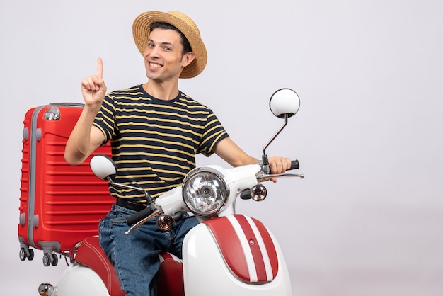 Widok z przodu uśmiechniętego młodego człowieka w słomkowym kapeluszu na motorowerze zaskakującym pomysłem