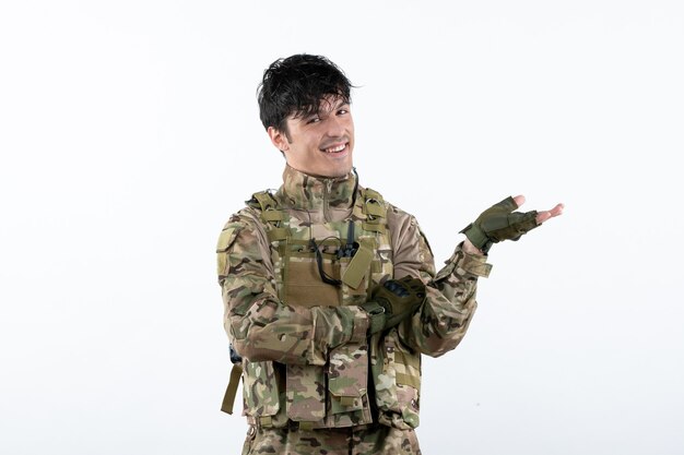 Widok z przodu uśmiechniętego młodego żołnierza w mundurze wojskowym na białej ścianie