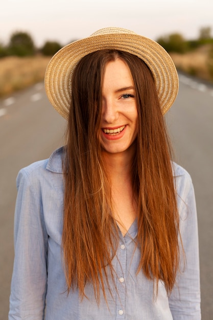 Widok z przodu uśmiechniętej kobiety w kapeluszu stwarzających o zachodzie słońca na drodze