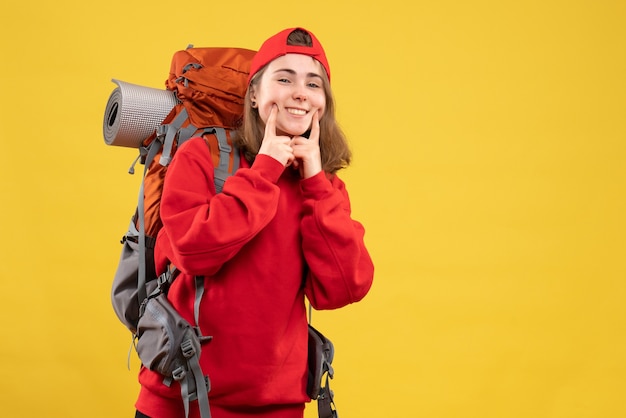 Widok z przodu uśmiechnięty młody turysta z plecakiem i czerwoną czapką kładąc palec wskazujący na jej policzek