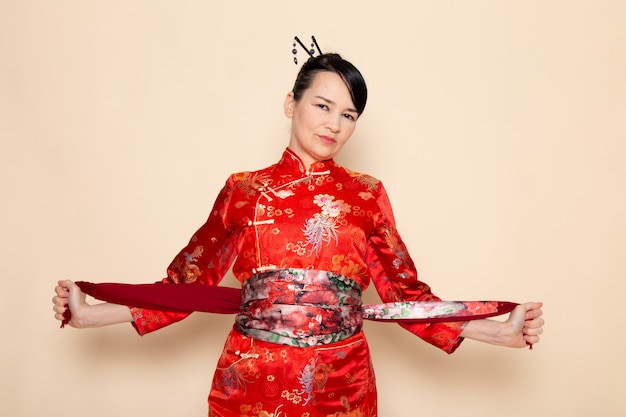 Bezpłatne zdjęcie widok z przodu wykwintna japońska gejsza w tradycyjnej czerwonej japońskiej sukni pozuje elegancko z zaprojektowanym pasem na kremowej ceremonii japan