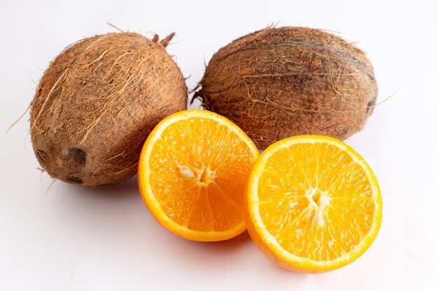 Widok z przodu z bliska świeże kokosy wraz z plasterkami pomarańczy na białej powierzchni