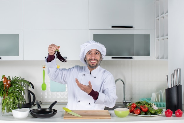 Widok z przodu zadowolony mężczyzna szef kuchni w mundurze trzymający bakłażana w kuchni