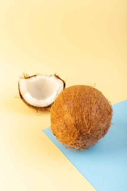 Widok z przodu zamknięte kokosy całe i pokrojone mleczny świeży mellow izolowany na kremowo-lodowo-niebieskim tle tropikalne owoce egzotyczne orzech