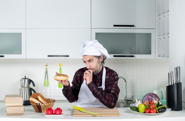 Widok z przodu zamyślonego męskiego szefa kuchni patrzącego na chleb w kuchni
