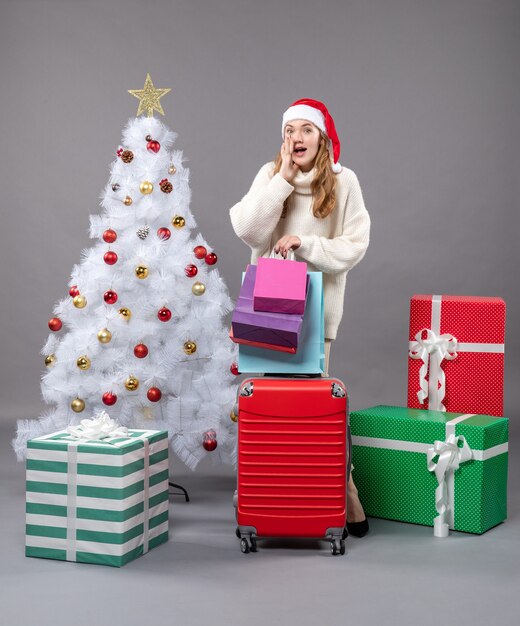 Widok z przodu zaskoczona blondynka z santa hat trzyma czerwoną walizkę i torby na zakupy