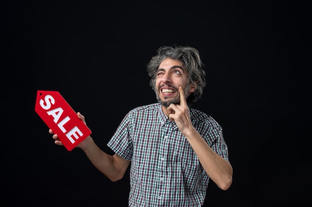 Bezpłatne zdjęcie widok z przodu zdziwionego mężczyzny zaskoczony pomysłem trzymającym czerwony znak sprzedaży na ciemnej ścianie